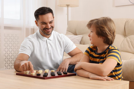 Father playing checkers with his son at table in room