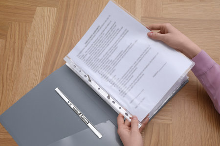 Woman putting punched pocket with document into file folder at wooden table, above viewの写真素材