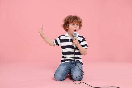 Cute little boy with microphone singing on pink backgroundの写真素材