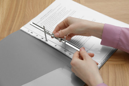 Woman fixing folder with punched pockets at wooden table, closeupの写真素材