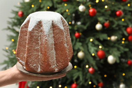 Woman holding delicious Pandoro cake decorated with powdered sugar near Christmas tree, closeup and space for text. Traditional Italian pastryの写真素材