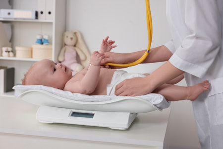 Pediatrician examining cute little baby with stethoscope and weighting it in clinic, closeupの写真素材