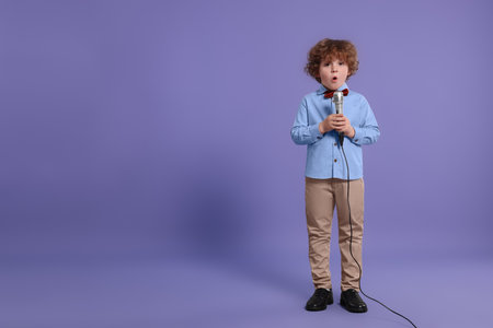 Cute little boy with microphone singing on violet background, space for textの写真素材