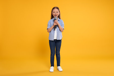 Cute little girl with microphone singing on yellow backgroundの写真素材