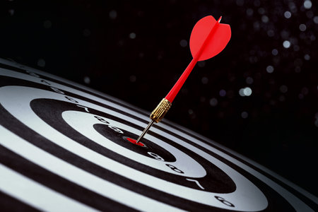 Dart board with red arrow hitting target against black background, bokeh effect