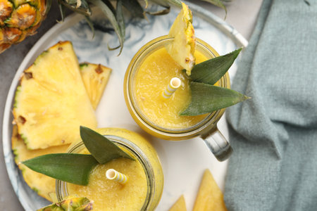 Tray with tasty pineapple smoothie and sliced fruit on table, flat lay