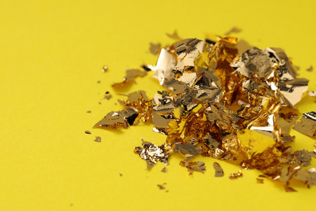 Many pieces of edible gold leaf on yellow background, closeupの写真素材