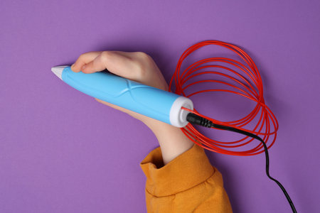 Boy drawing with stylish 3D pen on purple background, top view