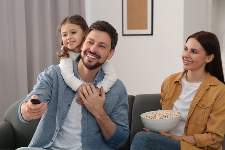 Happy family watching movie at home. Father changing TV channels with remote control
