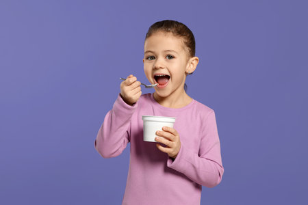 Girl eating tasty yogurt on violet backgroundの写真素材