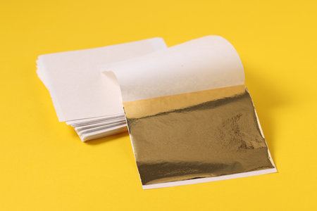Edible gold leaf sheets on yellow background, closeupの写真素材