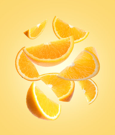 Juicy orange slices flying on pale golden backgroundの写真素材