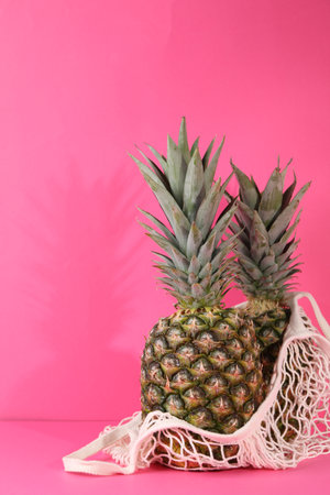 Whole ripe pineapples and net bag on pink backgroundの写真素材