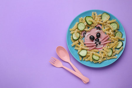 Creative serving for kids. Plate with cute bear made of tasty pasta, vegetables and sausage on violet background, flat lay. Space for textの写真素材