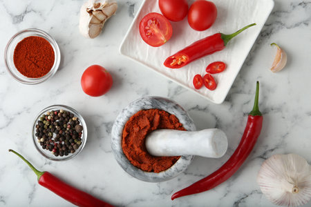 Red curry paste in mortar and ingredients on white marble table, flat layの写真素材