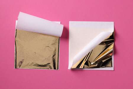 Edible gold leaf sheets on pink background, flat lay