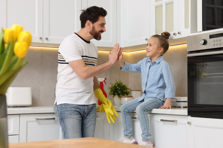 Spring cleaning. Father and daughter giving high five in kitchenの写真素材