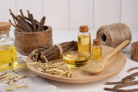 Dried sticks of licorice roots, powder and essential oil on white wooden tableの写真素材