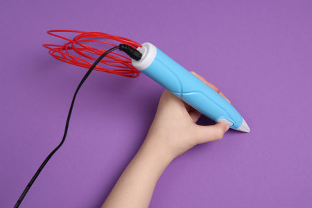 Boy drawing with stylish 3D pen on purple background, top view