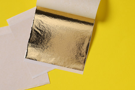 Edible gold leaf sheets on yellow background, top viewの写真素材