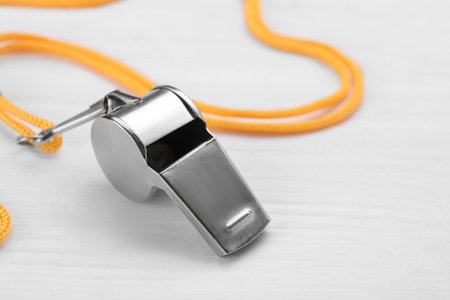 One metal whistle with cord on white wooden table, closeup