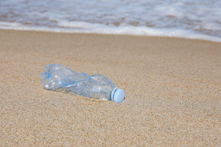 Used plastic bottle on sand near water. Recycling problemの写真素材