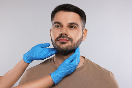 Endocrinologist examining thyroid gland of patient on light gray background, closeupの写真素材