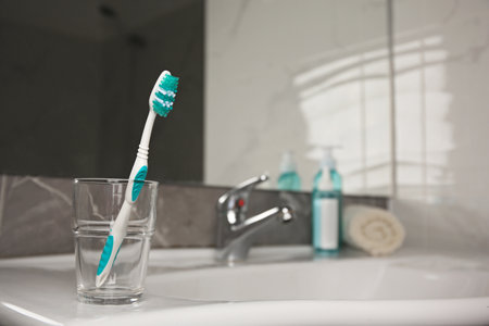 Light blue toothbrush in glass holder on washbasinの写真素材