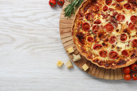 Delicious homemade quiche and ingredients on white wooden table, flat lay. Space for text