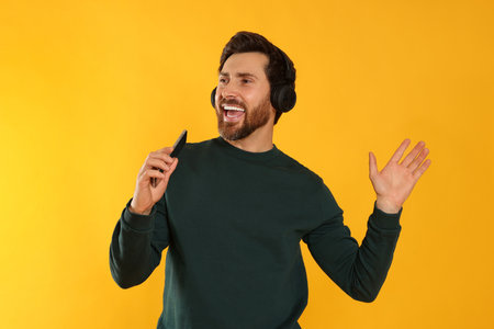 Happy man listening music with headphones on yellow backgroundの写真素材