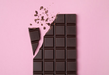 Broken dark chocolate bar on pink background, flat layの写真素材