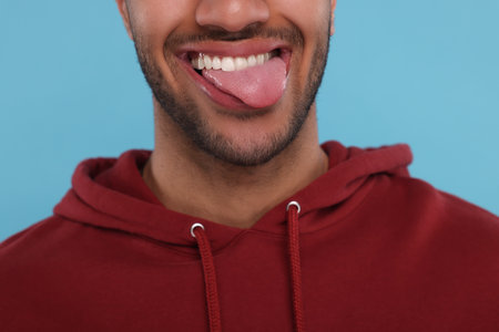 Happy man showing his tongue on light blue background, closeupの写真素材