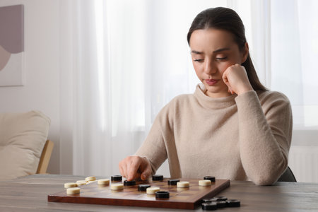 Playing checkers. Concentrated woman thinking about next move at table in room, space for text