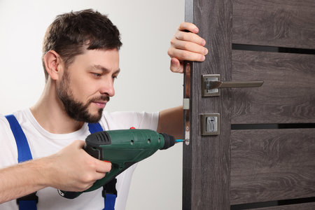 Worker with screw gun repairing door lock indoorsの写真素材