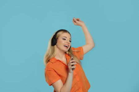 Happy woman in headphones enjoying music and singing into smartphone on light blue backgroundの写真素材
