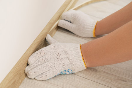 Man installing plinth on laminated floor in room, closeupの写真素材