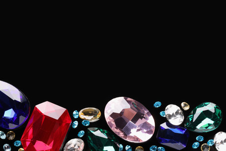Different beautiful gemstones for jewelry on black background, flat lay. Space for textの写真素材