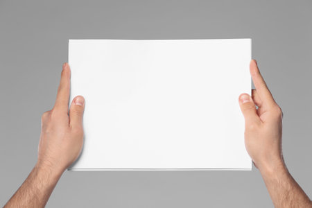 Man holding sheet of paper on gray background, closeup. Mockup for designの写真素材