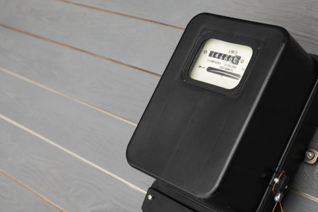 Black electric meter on gray wooden wall, space for text. Measuring device
