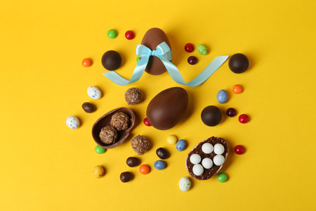 Tasty chocolate eggs and candies on yellow background, flat lay