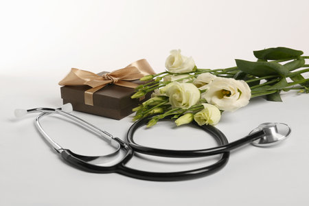 Stethoscope, gift box and eustoma flowers on white background. Happy Doctor's Dayの写真素材