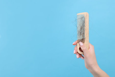 Woman holding comb with lost hair on light blue background, closeup and space for text. Alopecia problemの写真素材