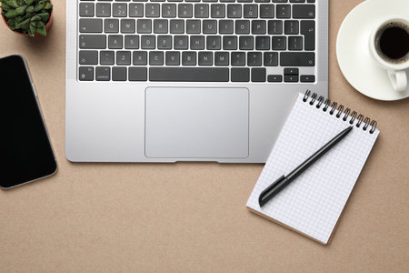 Modern laptop, notebook and cup of coffee on beige table, flat lay. Space for textの写真素材