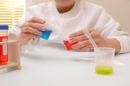 Girl mixing colorful liquids at white table indoors, closeup. Chemical experiment set for kidsの写真素材