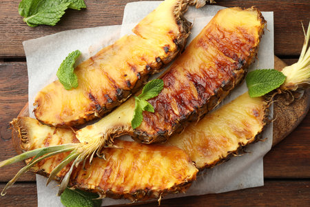 Tasty grilled pineapple pieces and mint leaves on wooden table, flat layの写真素材