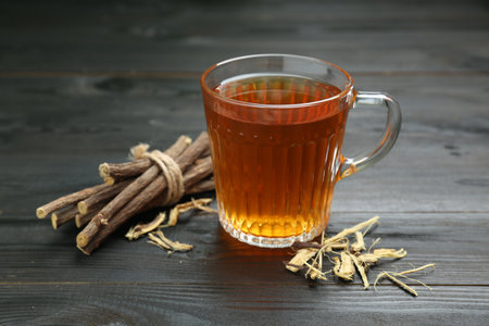Aromatic licorice tea in cup and dried sticks of licorice root on black wooden tableの写真素材