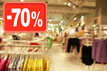 Sale sign and blurred view of fashion store with clothes