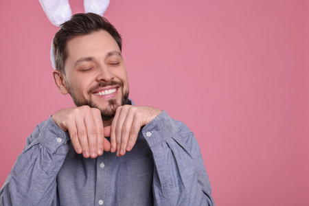 Happy man wearing bunny ears headband on pink background, space for text. Easter celebrationの写真素材