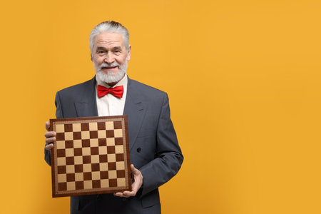 Man with chessboard on orange background, space for text. Intellectual gameの写真素材