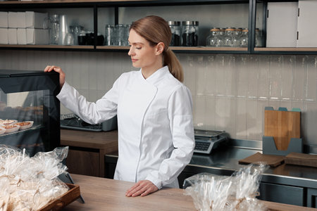 Professional baker at cashier desk near showcase in storeの写真素材